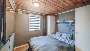 Un dormitorio con cama, ventana con persianas, estante con libros e iluminación en el techo.