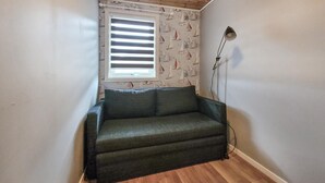 Una habitación pequeña con un sofá verde oscuro, una ventana con persianas y una lámpara de pie.