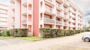 Un edificio residencial de varios pisos con balcones, una columna central roja y un estacionamiento.