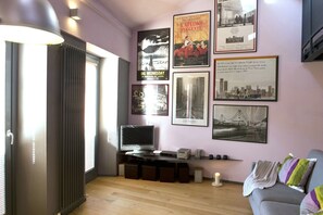 A living room with a TV, posters, a sofa, and a window with blinds. - Casa Rossa - My Home In Como (Cernobbio)