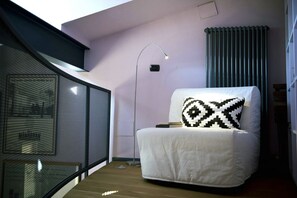 A modern room with a white armchair, a floor lamp, a radiator, and a view through a glass partition. - Casa Rossa - My Home In Como (Cernobbio)