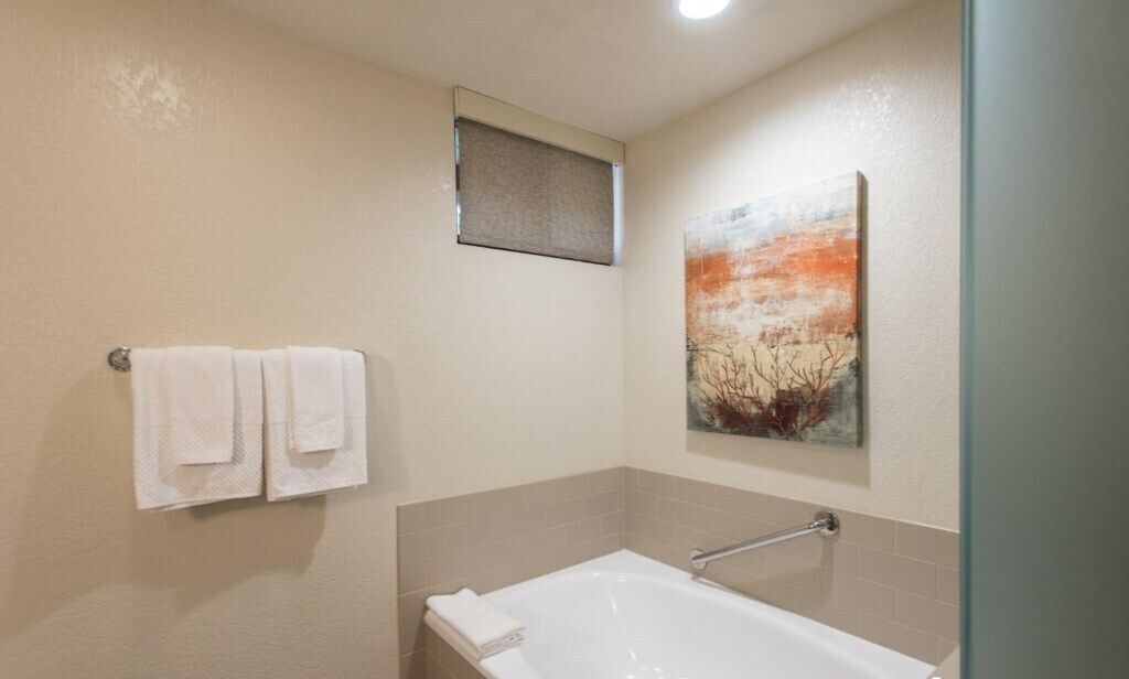 A bathroom with a bathtub, two towels on a rack, and a painting on the wall.
