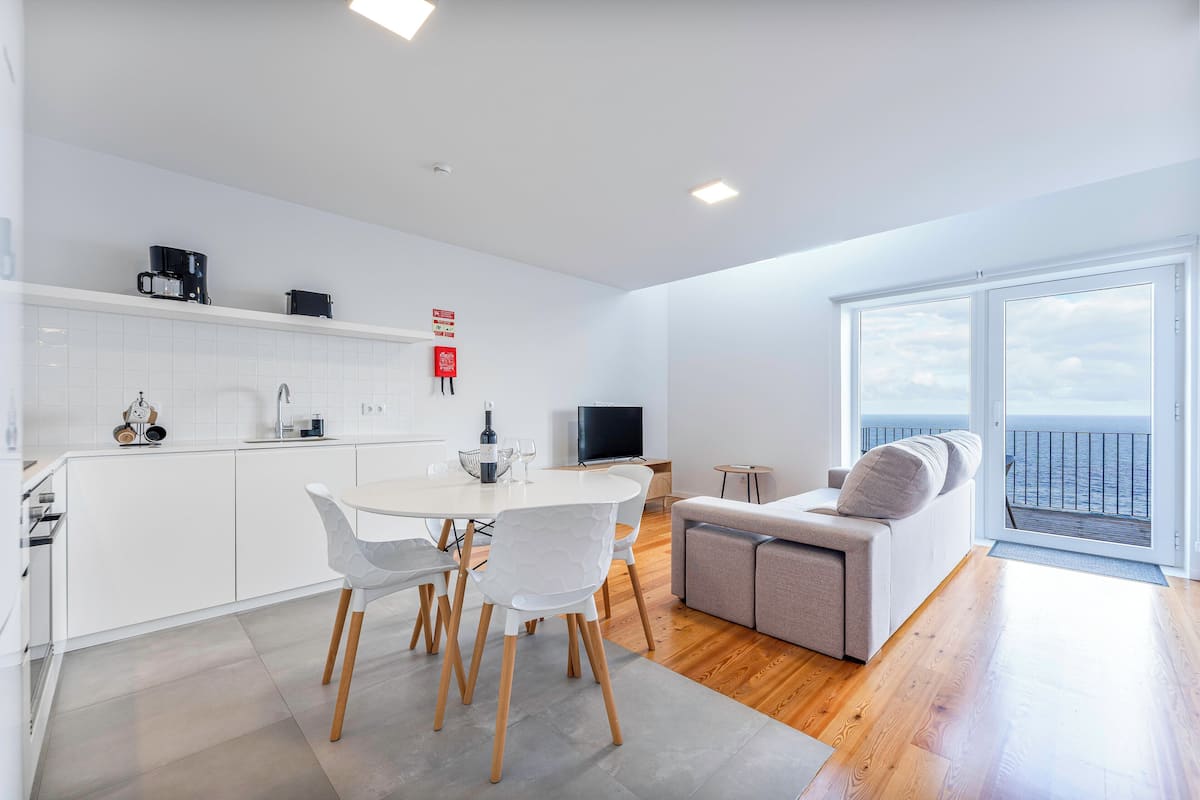 Um apartamento moderno com cozinha, sala de jantar e varanda com vista para o mar.
