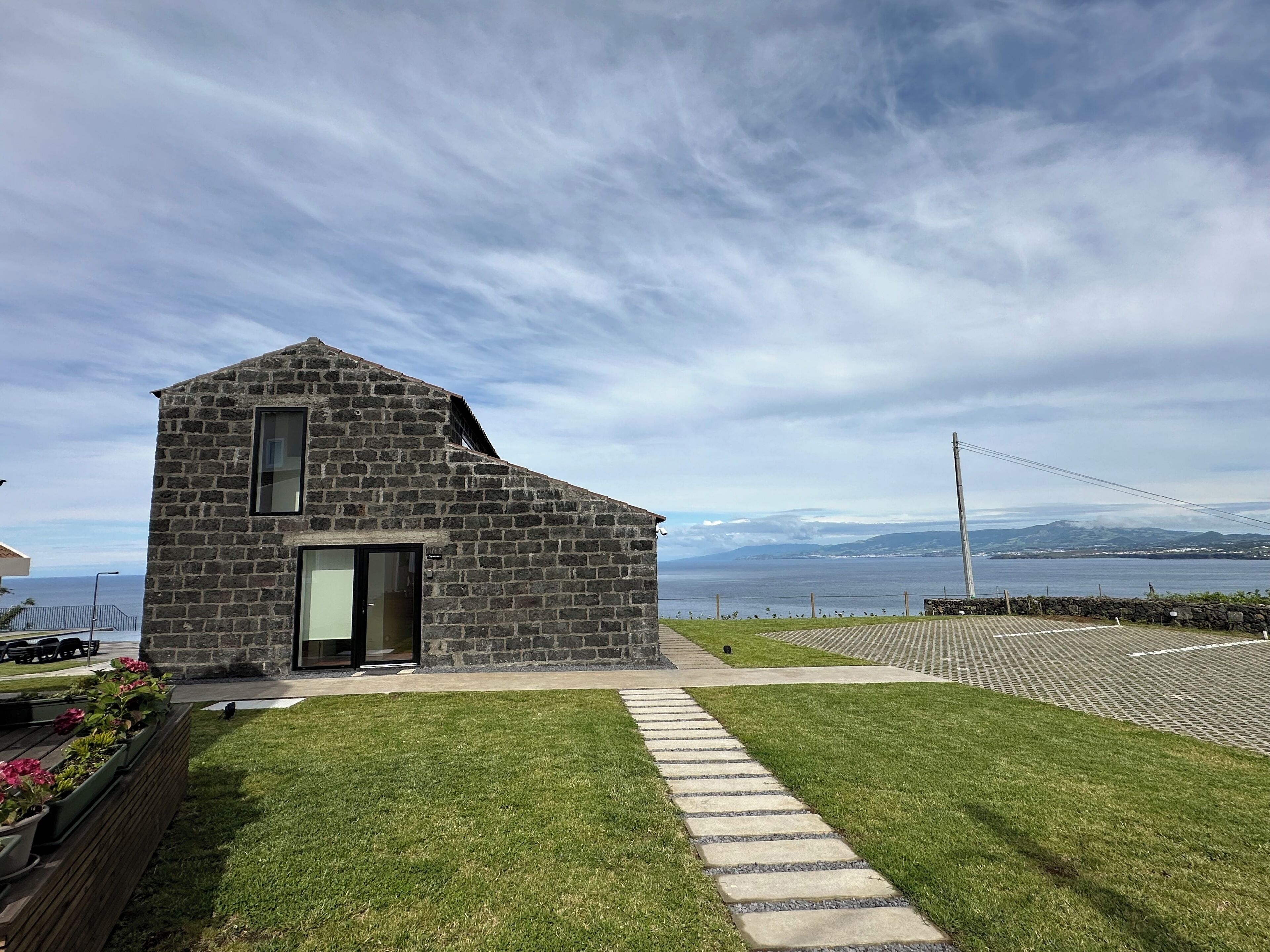 A stone building with a sloped roof and a glass door, located near a body of water with a view of distant mountains.