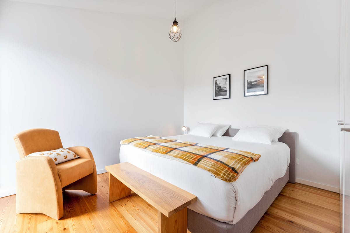 Um quarto moderno com uma cama, uma cadeira, um banco e duas imagens emolduradas na parede.