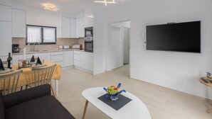 A modern kitchen with white cabinets, a dining area with a table set for two, and a flat-screen TV mounted on the wall.