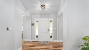 Un pasillo con suelo de madera, paredes blancas y una puerta blanca con paneles de vidrio esmerilado.
