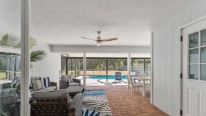 Un patio interior con mobiliario de mimbre, un ventilador de techo y vista a una piscina.