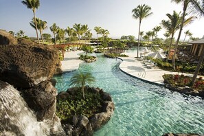 Poolbereich eines Resorts mit klarem Wasser, Palmen und Liegestühlen.