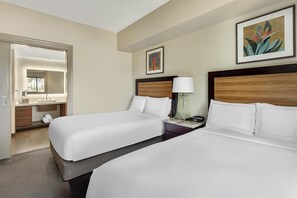 Ein Hotelzimmer mit zwei Betten, einem Badezimmer mit Spiegel und Bildern an den Wänden.