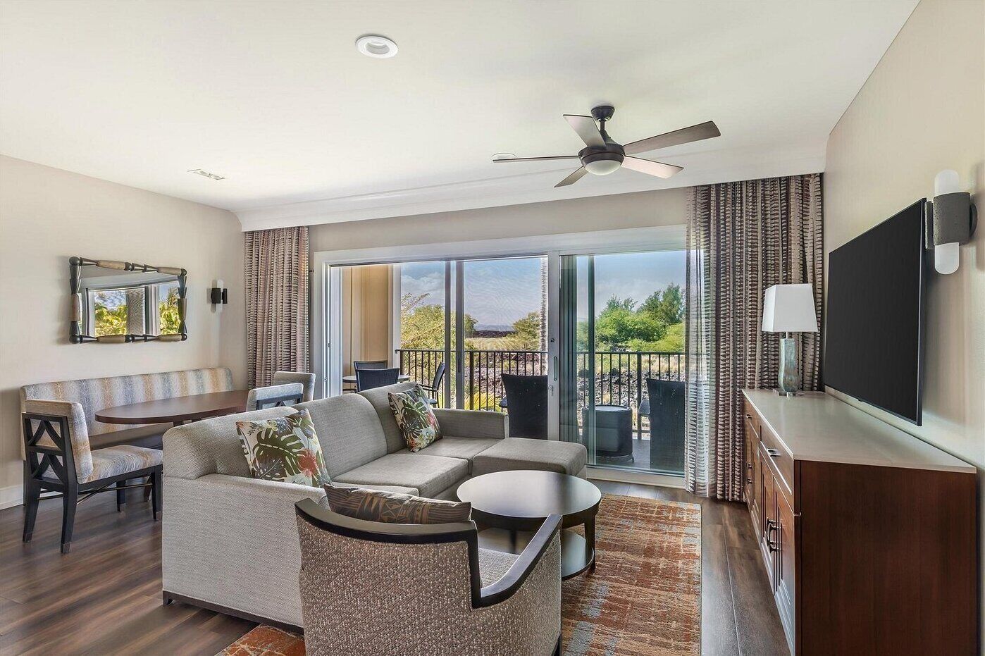 A modern living room with a sofa, a dining table, a TV, and a balcony with a view.