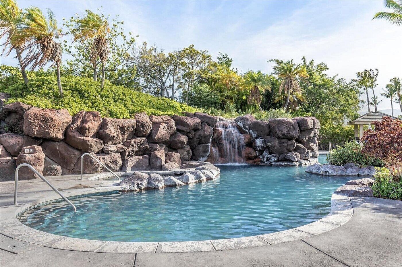 A pool with a waterfall, surrounded by rocks and palm trees.