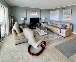 Sala de estar com sofá, poltrona, mesa de centro, televisão e objetos decorativos.