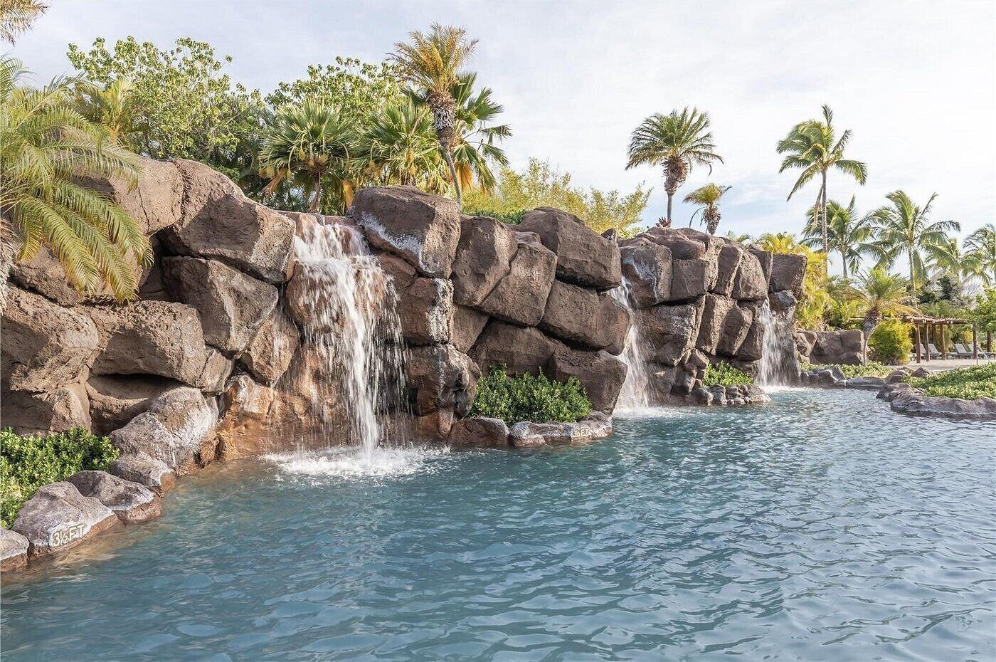 A pool with multiple waterfalls, surrounded by large rocks and palm trees.