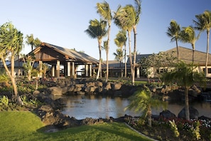 A resort with a pool, palm trees, and a building with a thatched roof.
