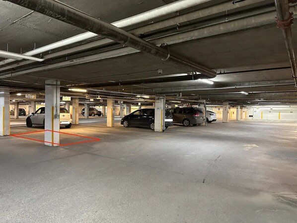 Un estacionamiento subterráneo de varios niveles con pilares de concreto, espacios de estacionamiento delimitados e iluminación en el techo.