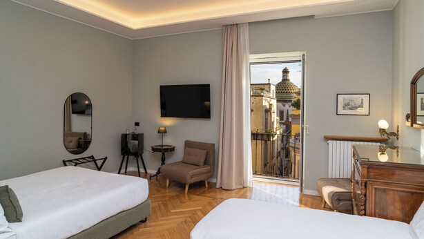 A hotel room with two beds, a TV, a chair, a desk, and a balcony with a view of a building. - Deluxe Spaccanapoli (Naples)