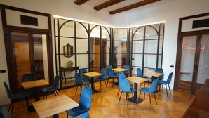 A modern dining area with wooden tables and blue chairs, featuring a glass partition wall and wooden ceiling beams. - Deluxe Spaccanapoli (Naples)