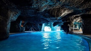 Une piscine intérieure dotée d’un plafond en forme de grotte rocheuse et agrémentée d’une cascade.