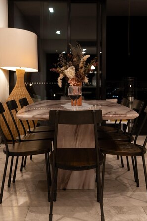 Une table de salle à manger ronde, entourée de six chaises, un vase rempli de fleurs et un verre à vin.