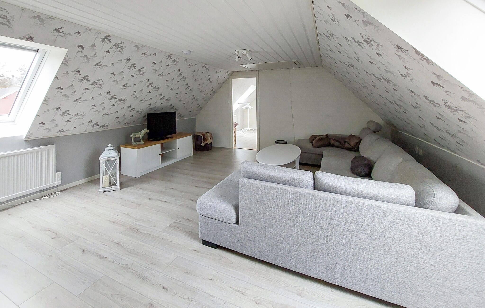 A loft-style room with a grey sofa, a small white table, and a television on a white cabinet.