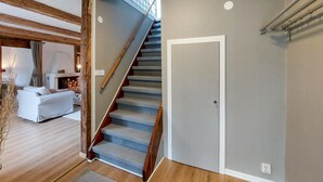 Una escalera conduce a un rellano con una puerta, un sofá y una chimenea al fondo.