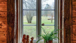 Ventana con marco de madera que da a un campo cubierto de hierba y árboles.