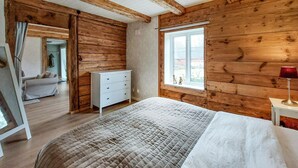 Un dormitorio con paredes de madera, una cama con colcha, un aparador y una ventana con vistas.