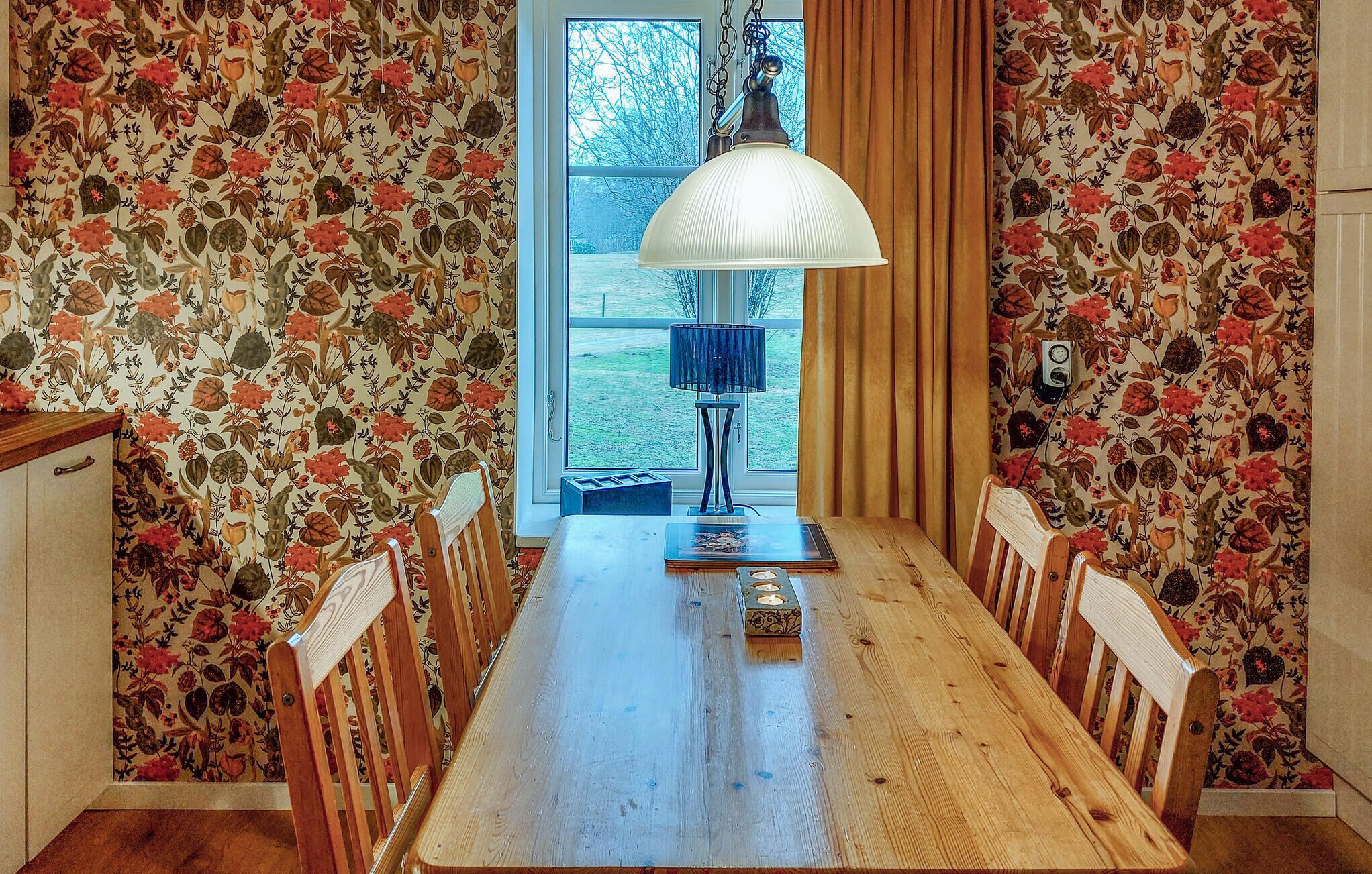 Une salle à manger avec une table en bois, des chaises, une lampe et un papier peint à motifs floraux.