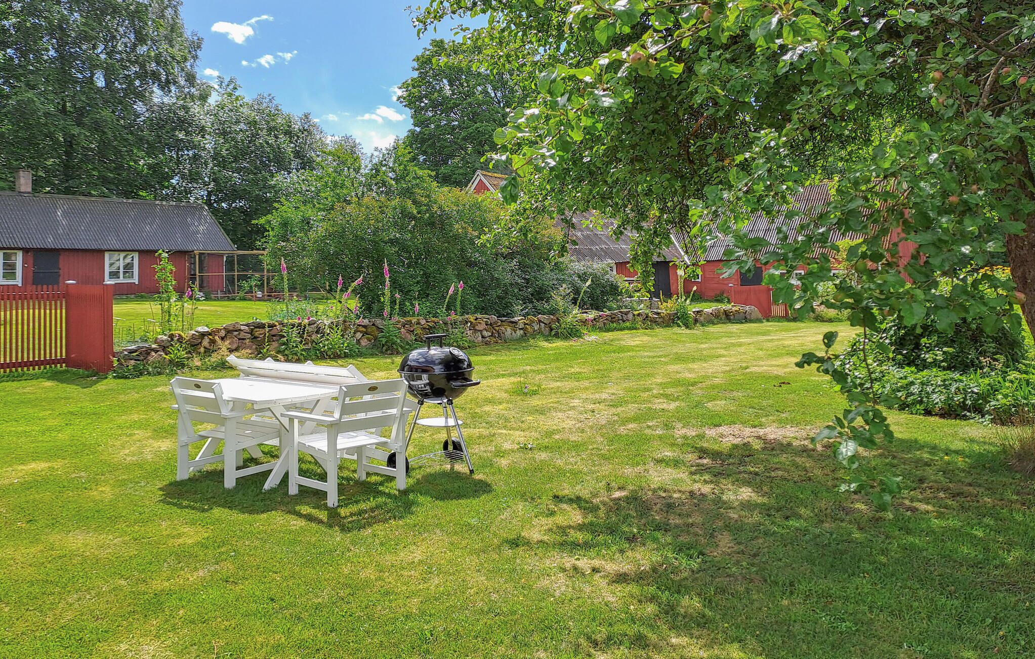 A grassy backyard with a barbecue grill, a white table and chairs, and a stone wall.