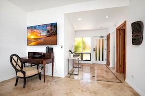 A modern interior with a desk, chair, artwork, and a view to a balcony.