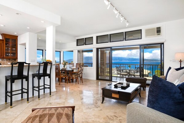 A spacious living area with a balcony overlooking a scenic view, a kitchen with high ceilings and large windows, and modern furnishings.