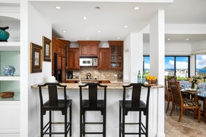 A modern kitchen with wooden cabinets, a granite countertop, and a bar area with three stools.