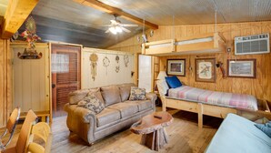 Een gezellig interieur van een chalet met houten plafond, een plafondventilator, een bank, een bed en een kleine tafel.