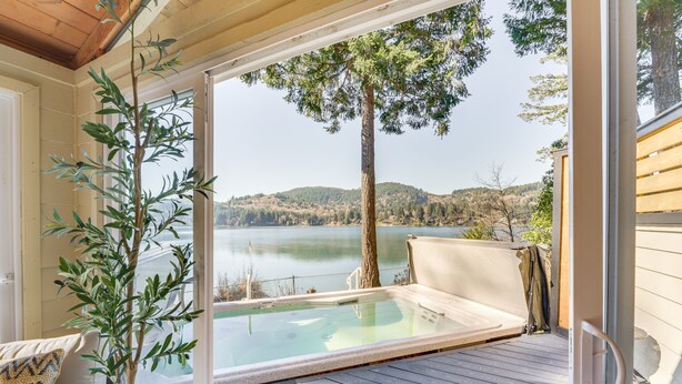 Un'area prendisole in legno con una porta vetrata che dà su una vasca idromassaggio con vista sul lago.