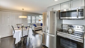Una cocina moderna con electrodomésticos de acero inoxidable, un comedor con mesa y sillas, y una sala de estar con sofá y ventana.
