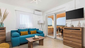 A modern living room with a blue sofa, wooden coffee table, and a TV mounted on the wall. - Holiday apartment with panoramic sea views (Klimno)
