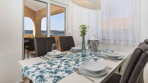 A dining area with a table set for four, a vase with flowers, and a view of the sea through large windows. - Holiday apartment with panoramic sea views (Klimno)