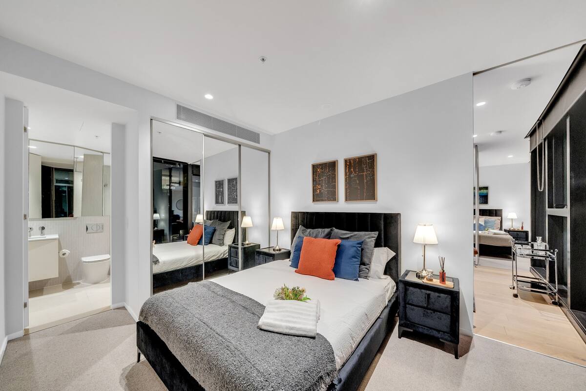 A modern bedroom with a large bed, bedside tables, a mirror, and a view into the bathroom.