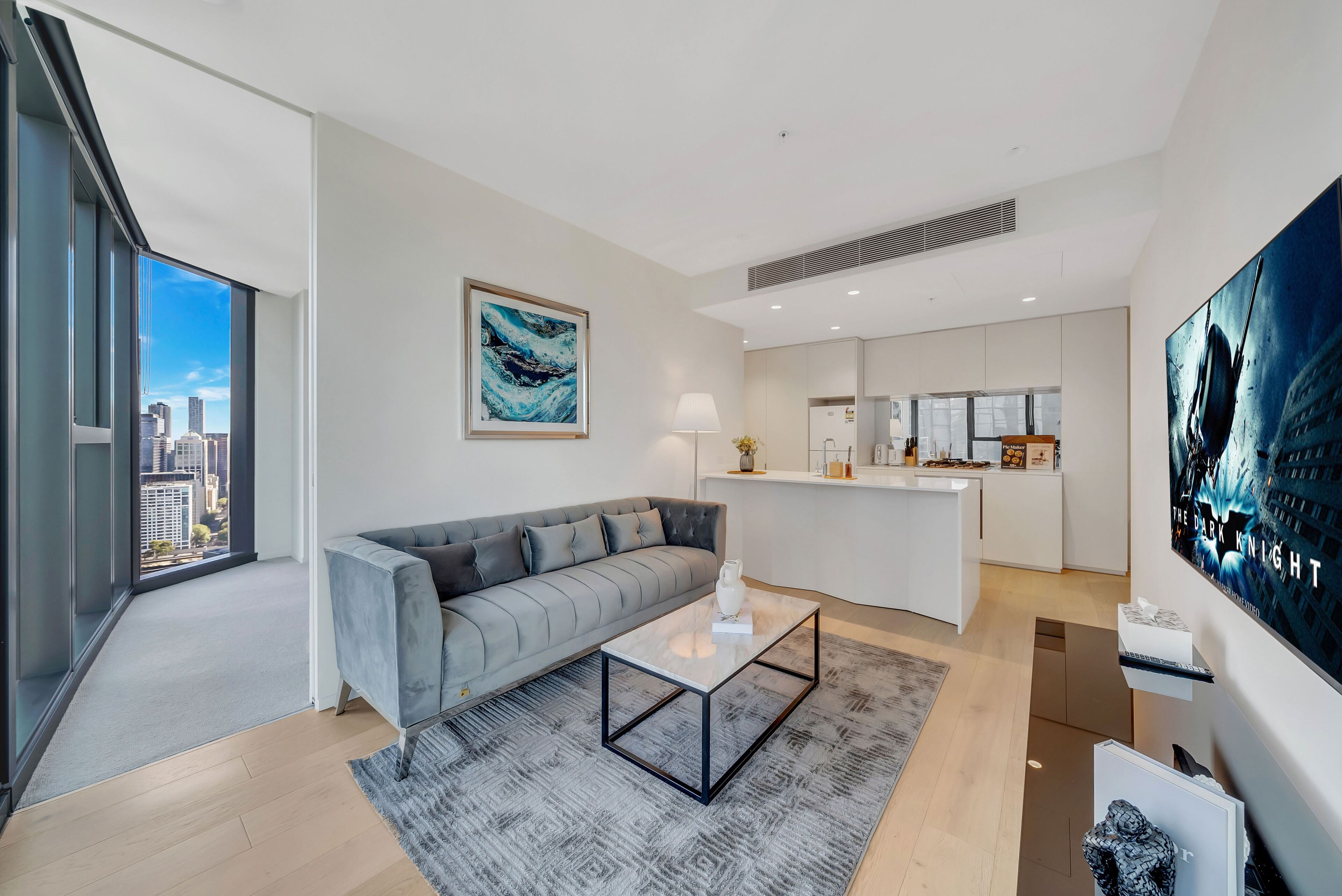 A modern living room with a gray sofa, a coffee table, and a city view through large windows.