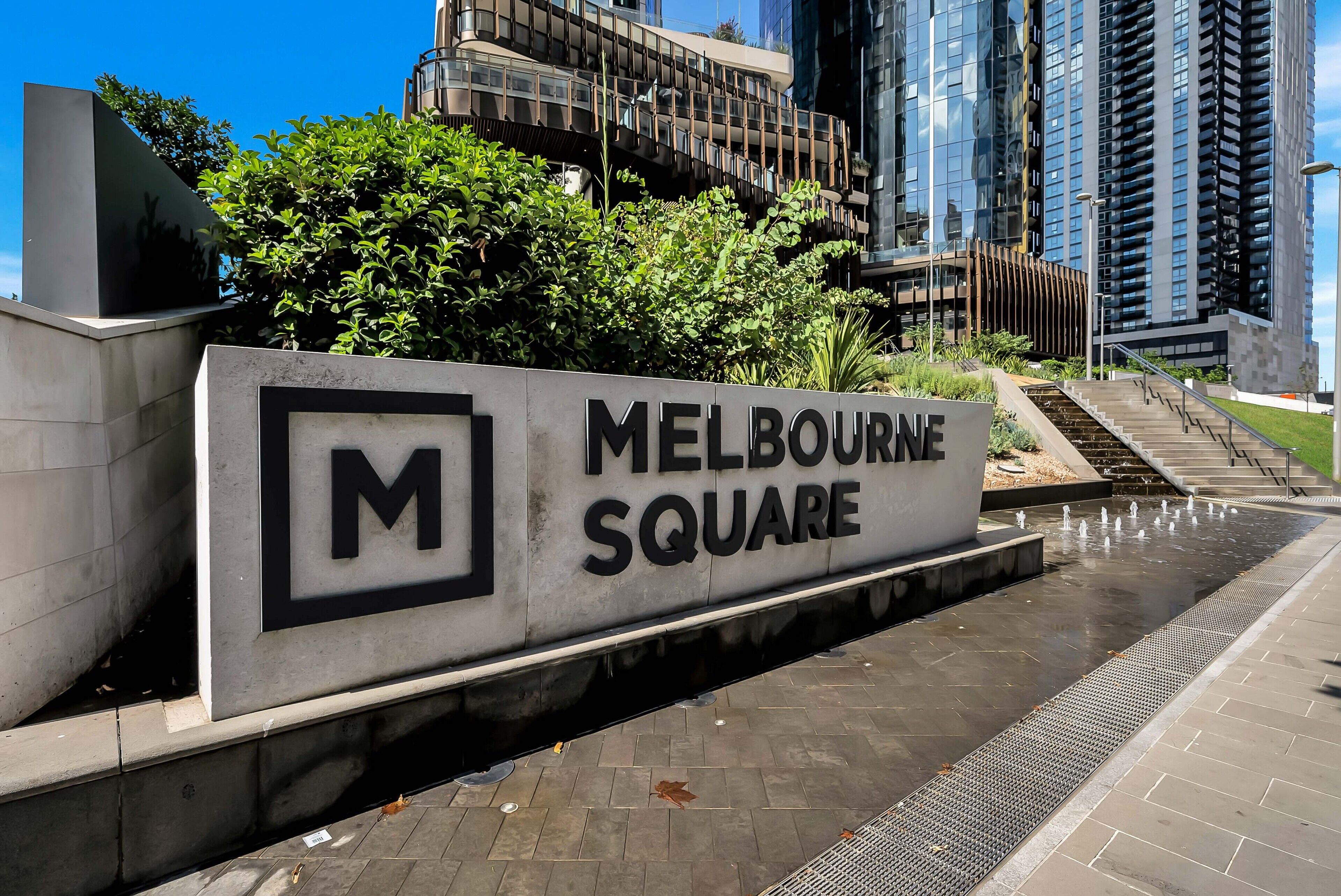 A sign for Melbourne Square with a modern building in the background.