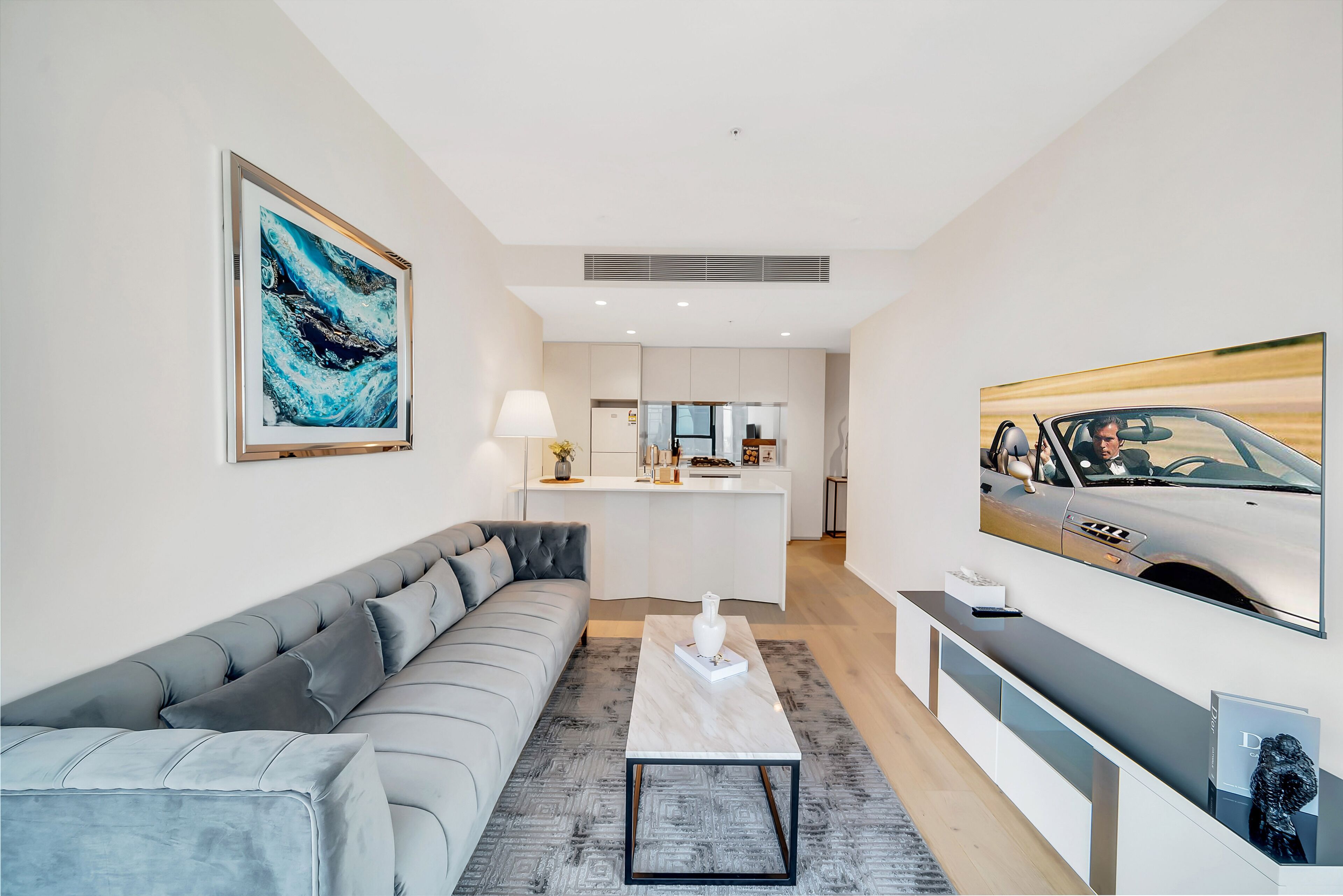 A modern living room with a grey sofa, a marble coffee table, and a kitchen in the background.