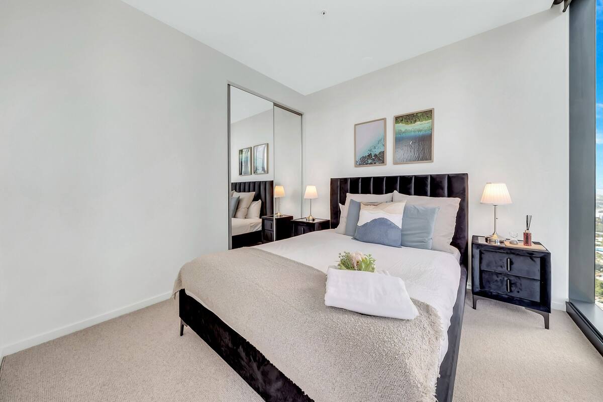 A modern hotel room with a large bed, a nightstand, a mirror, and artwork on the wall.