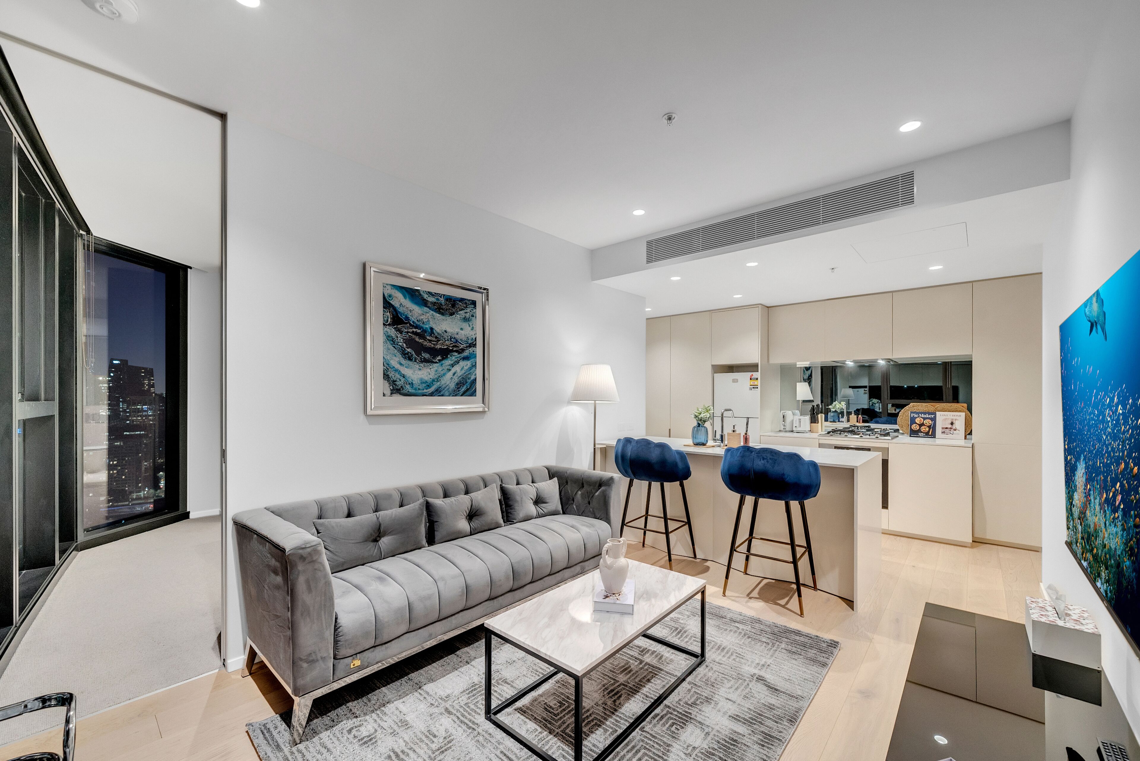 Un salon moderne avec un canapé gris, une table basse et une vue sur la ville par une grande fenêtre.