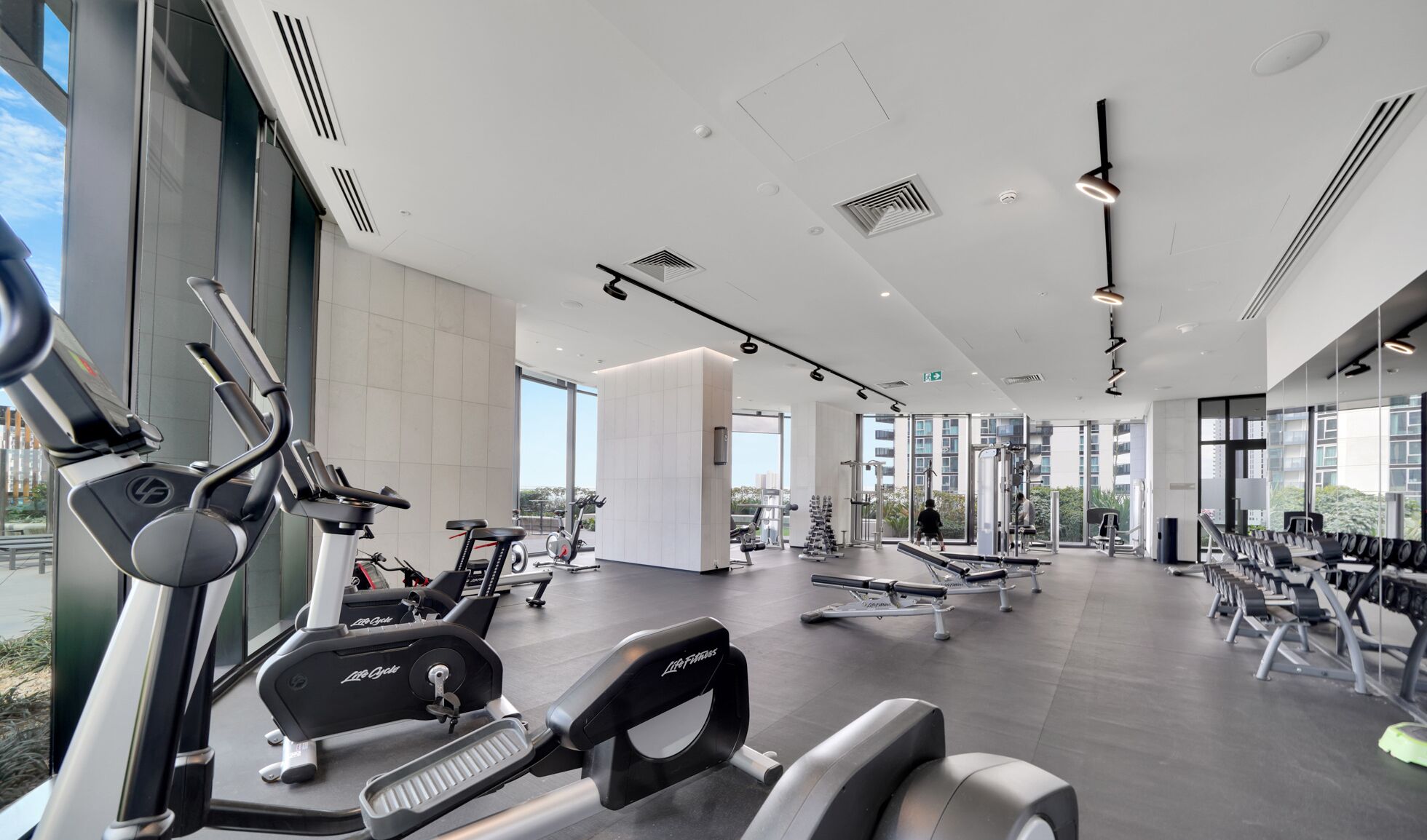 A modern gym with various exercise equipment, large windows, and a clean, spacious layout.