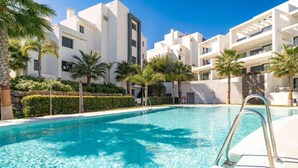 Une piscine à l’eau d’un bleu cristallin, entourée de bâtiments blancs et de palmiers.