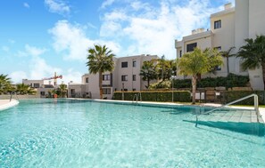 A clear swimming pool with a metal ladder, surrounded by modern buildings and palm trees. - Gorgeous apartment in Estepona with swimming pool (Estepona)