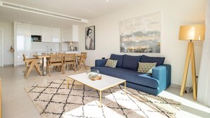 Un salon moderne avec un canapé bleu, une table basse et un coin repas avec des chaises en bois.