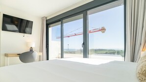 Une chambre d’hôtel avec un grand lit, un bureau avec une lampe, un téléviseur fixé au mur et une vue sur un chantier de construction avec une grue.