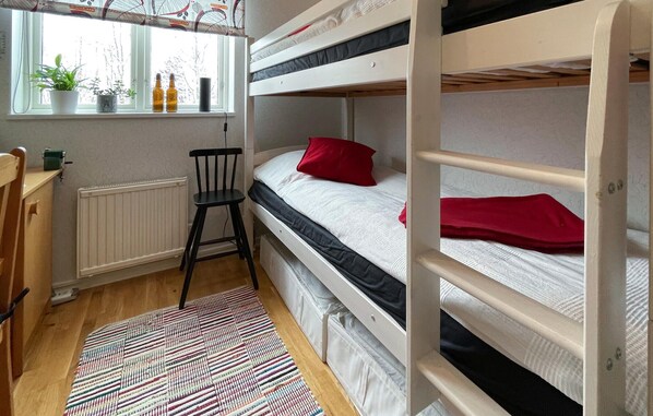 Une chambre de dortoir avec des lits superposés, un radiateur, une chaise, une fenêtre avec des plantes et un tapis à motifs.